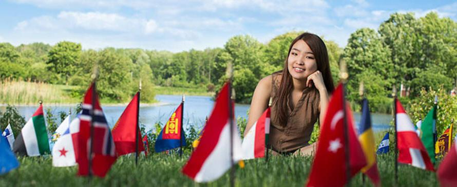 Student sitting in grass near flags.